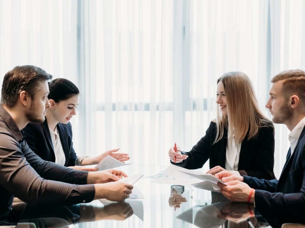 Four young professionals in business attire sitting around a glass table