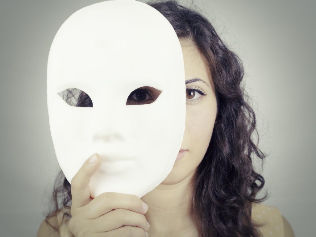 A woman with dark curly hair holding a plain white mask over one half of her face