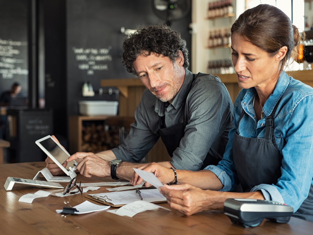 Two small business owners wearing aprons sitting at a wooden counter