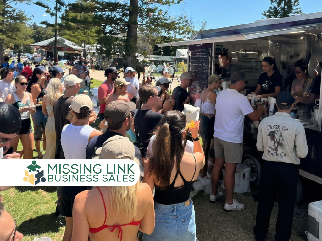 A large crowd of people gathered around a food truck on a sunny day at an outdoor event, with the "Missing Link Business Sales" logo positioned in the bottom left corner.